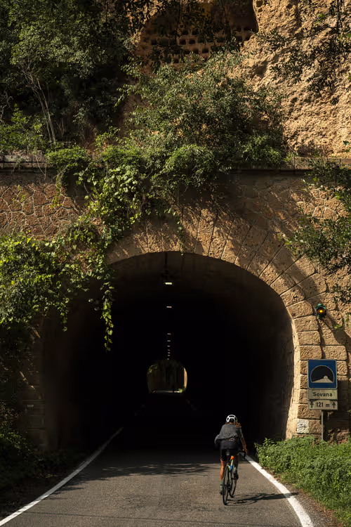 Female cyclist riding through a tunnel towards Sovana, Tuscany.
