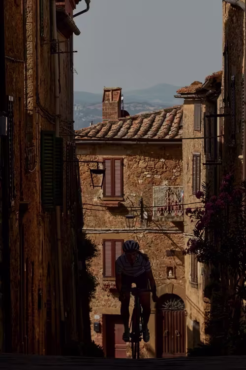 Female cyclist cycling through a small village in Tuscany.
