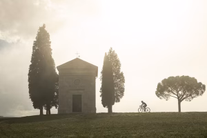 Silhouette of a female cyclist riding towards Chapel Vitaleta in Tuscany.