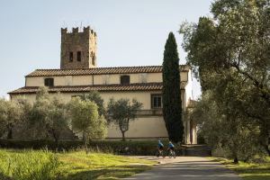 Two slow travelling cyclists riding past a church in Italy.
