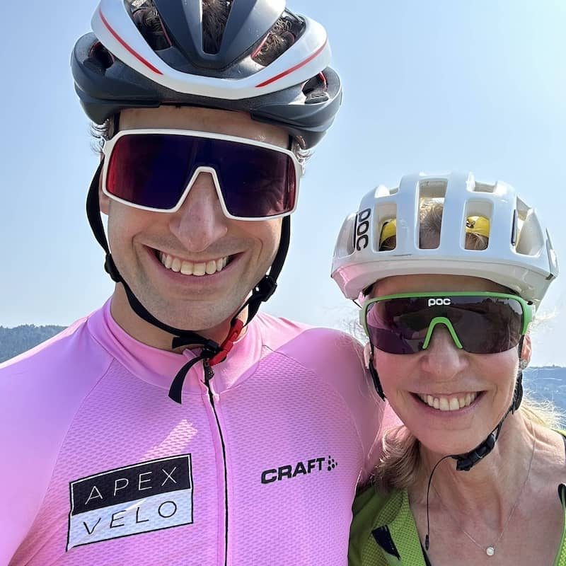 A son and mother wearing sunglasses, helmets, and cycling clothing.